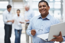 Middle aged business man using laptop with executives in the background